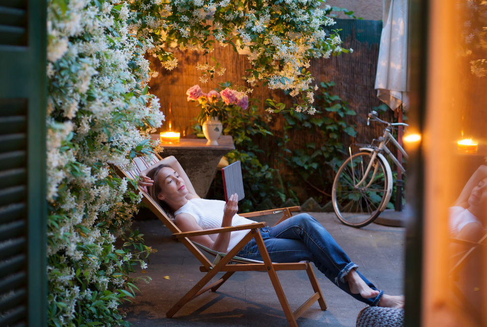 Woman Relaxing On Deck Chair In Backyard At Dusk, Reading On Digital Tablet