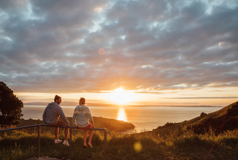 Friends Sitting On Railing Against Sky During Sunset