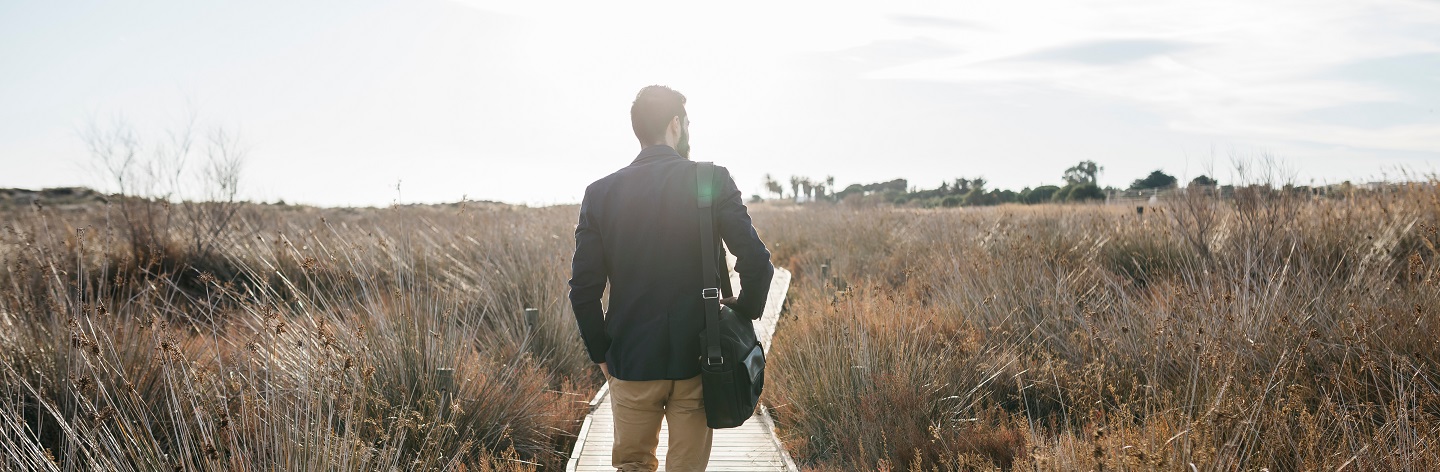 Rear View Of Mid Adult Man Walking On Boardwalk Against Sky