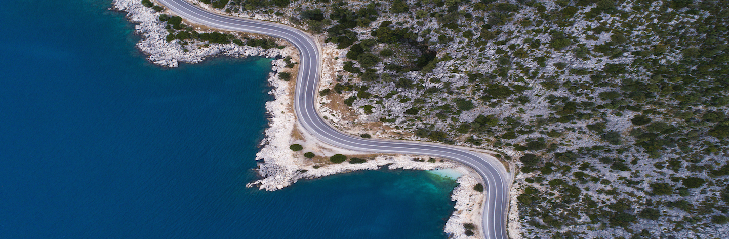 Aerial Landscape Of Coastline And A Road Seascape. Car Drives Down The Empty Asphalt Road Running Along The Sunny Mediterranean Shoreline Of Turkey. Tourist Car Cruises Down The Scenic Coastal Road .